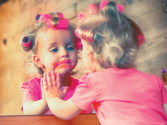 A child putting on makeup in front of mirror