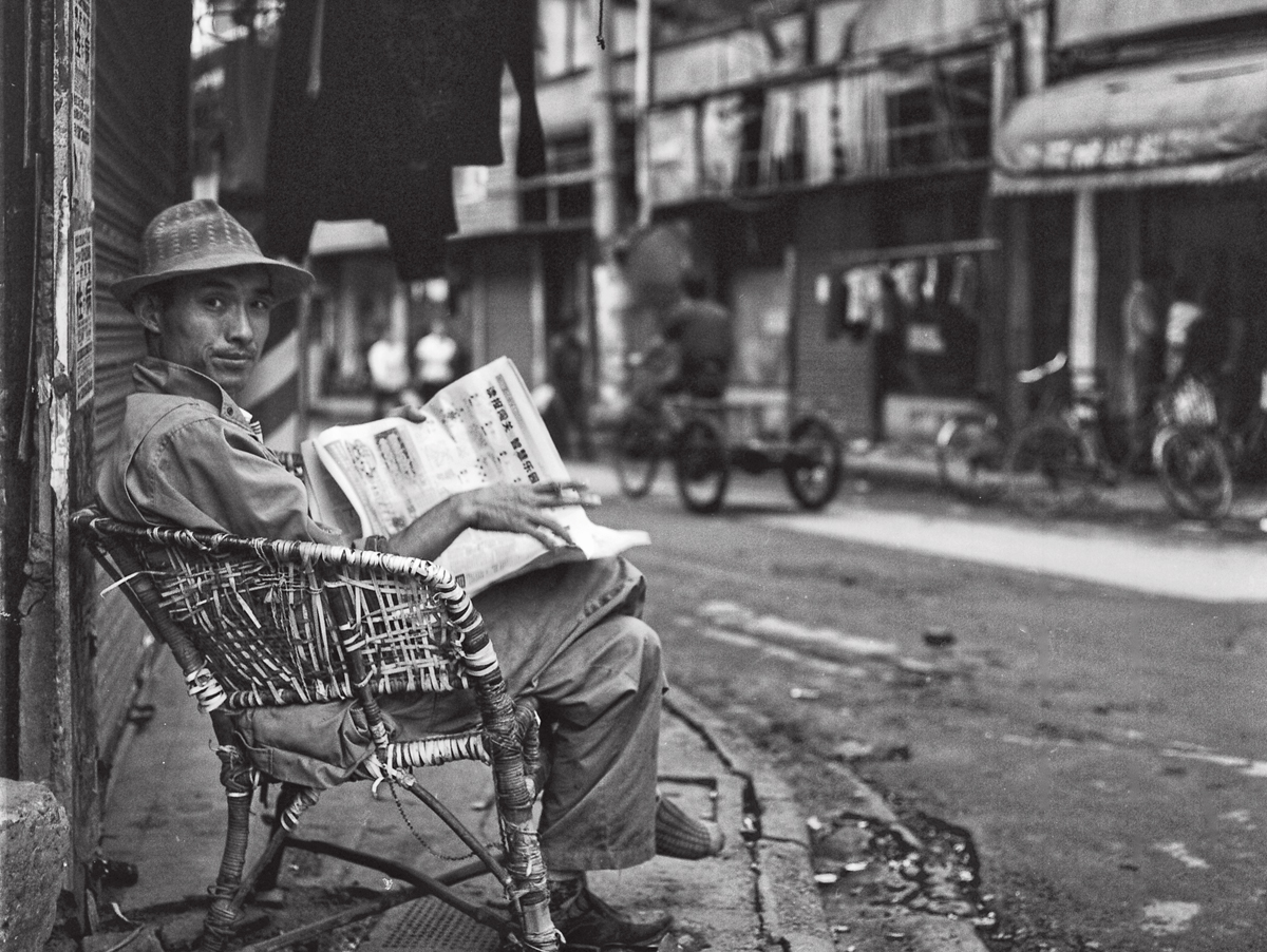 Photo of man reading newspaper on street in Shanghai, by Howard French