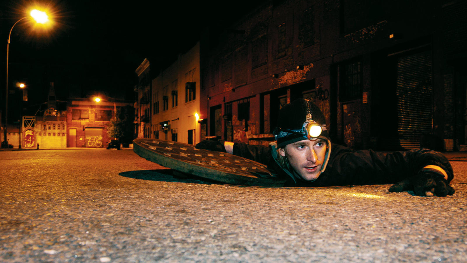 Photographer Steve Duncan crawling out of a man hole