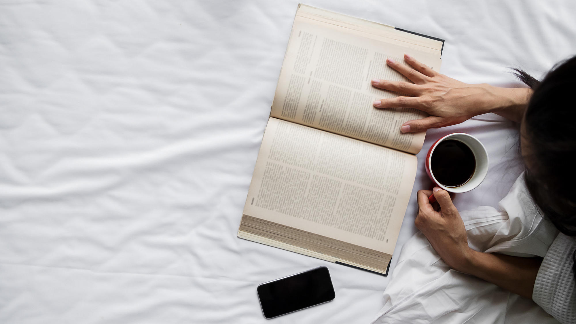 Photo of a person reading while drinking coffee