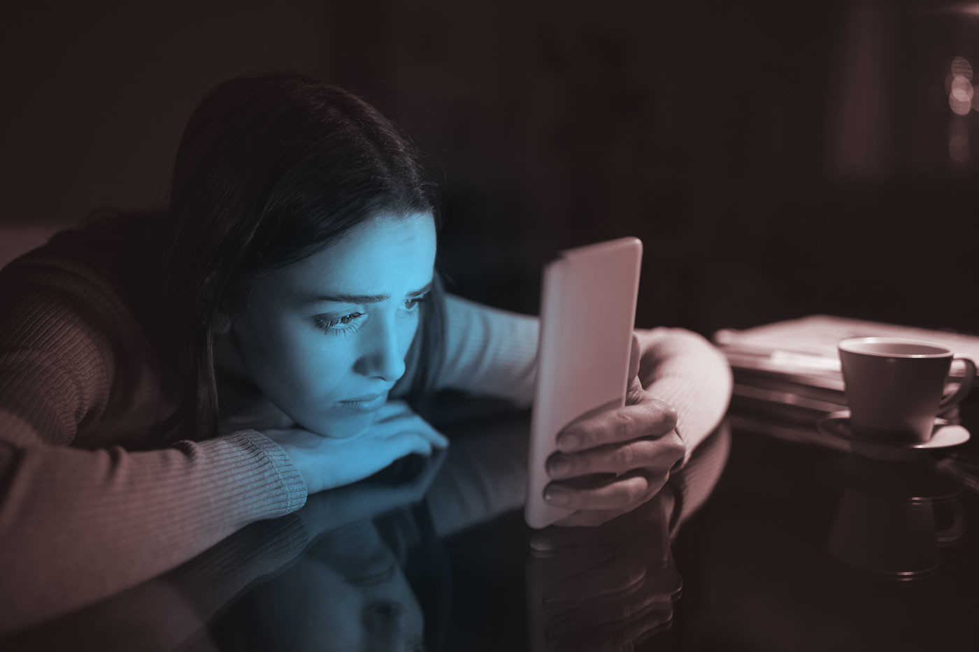 Photo of woman looking sadly at phone with blue light emanating