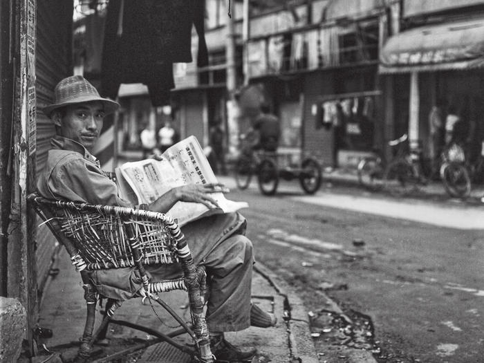 Photo of man reading newspaper on street in Shanghai, by Howard French