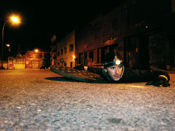 Photographer Steve Duncan crawling out of a man hole
