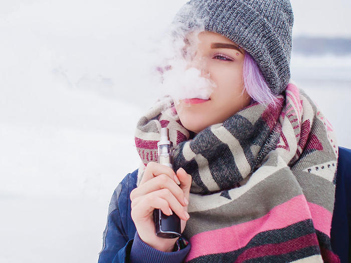 Young woman with purple hair and winter attire vaping with an electronic cigarette