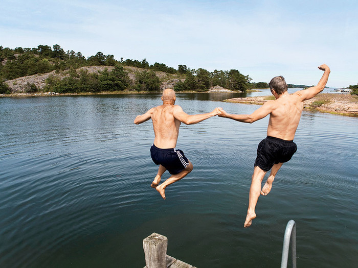 Photo of two older men jumping into a lake while holding hands