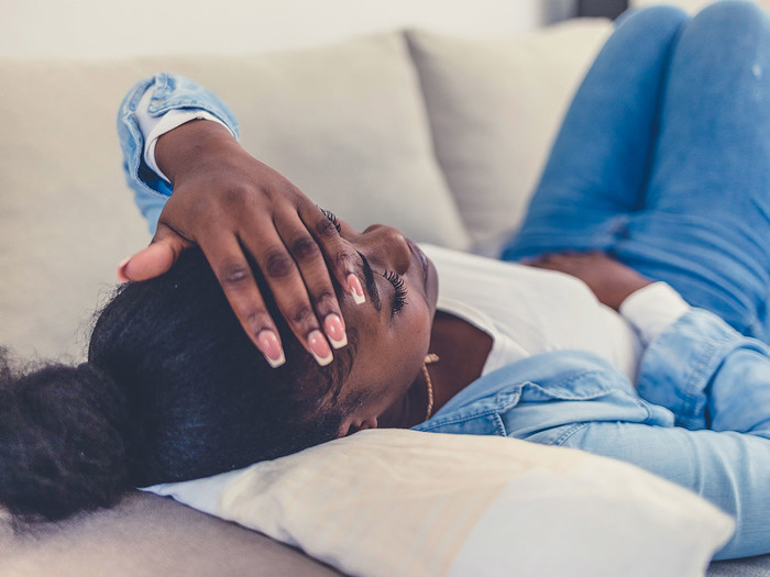 A woman laying on couch with her hand on head