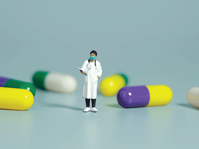 Graphic of a doctor figurine standing by giant pill capsules 