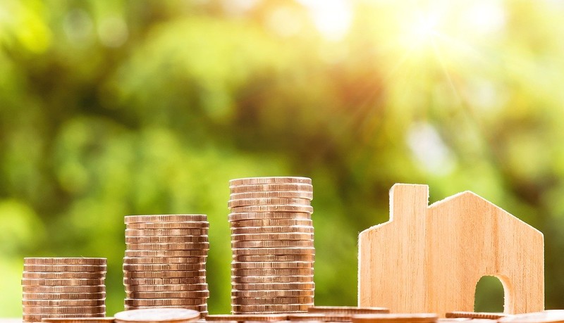 Stack of coins next to wooden model of a house