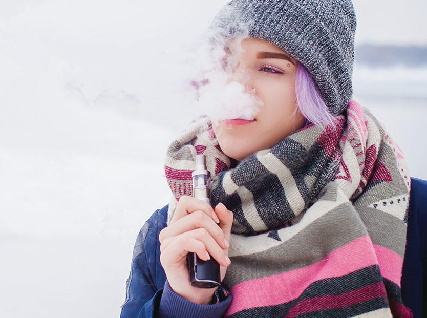 Young woman with purple hair and winter attire vaping with an electronic cigarette