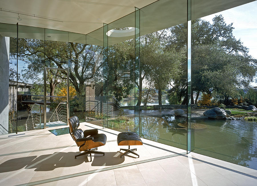Photo of an Eames lounge chair in a room with glass walls, facing nature