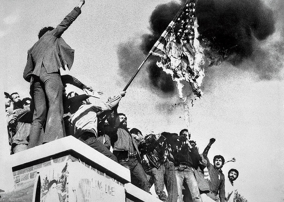 Demonstrators burn an American flag atop the wall of the US embassy in Tehran on November 9, 1979