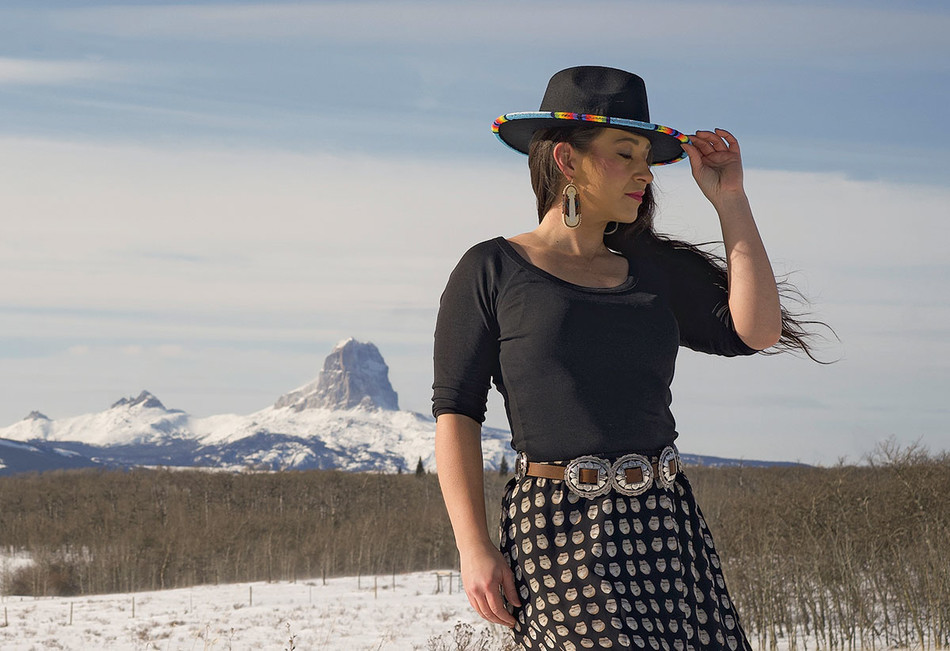 Mariah Gladstone, founder of Indigikitchen, photographed with hat outside in Babb, Montana with mountains in the background