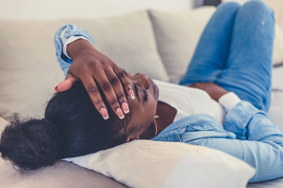 A woman laying on couch with her hand on head