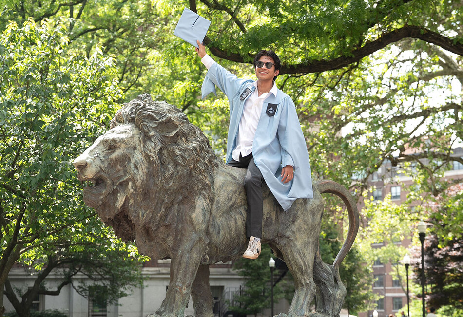 A Columbia graduate on top of the campus Lion sculpture at 2026 Commencement