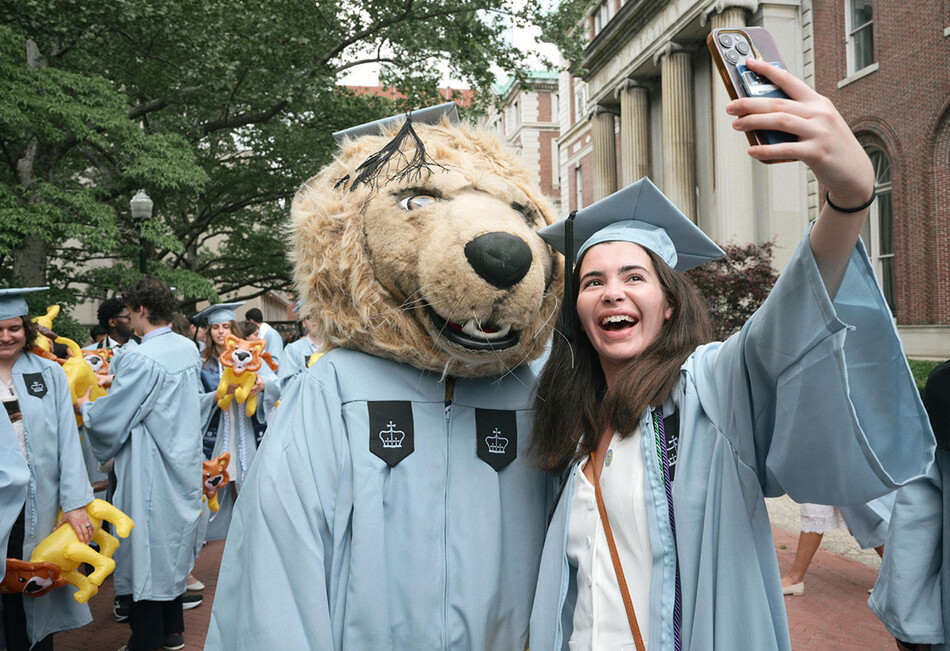 A Columbia graduate taking a selfie with the Roar-ee mascot at Commencement 2026